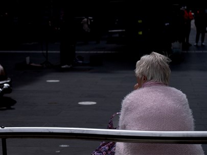 Woman in a pink cardigan sitting on her a park bench with her back to the camera.