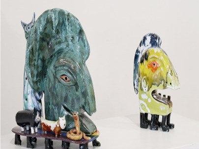 Two artworks of large heads mounted on pedestals with lots of animals around them