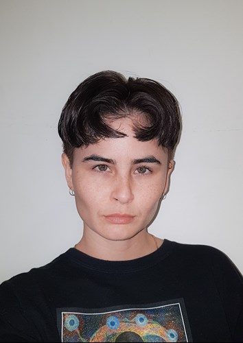 Ellen has high cheekbones and fair skin. They have brown eyes and black hair and pout for the camera. The haircut is very short parted in the middle.