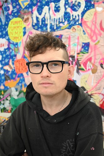 Headshot of Paul standing in front of some of their artwork