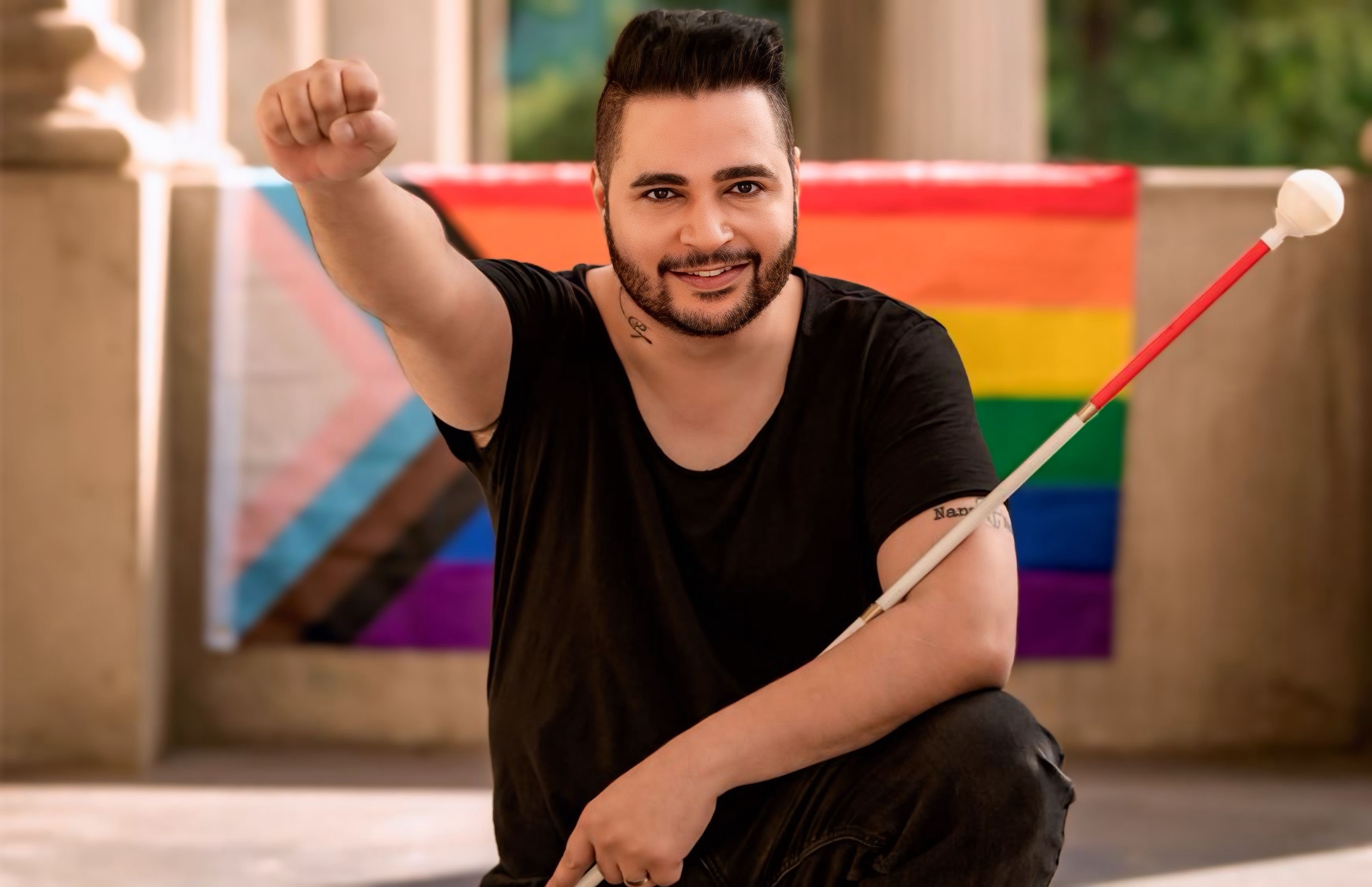 Karan with fist raised proudly squatting in front of a gay flag