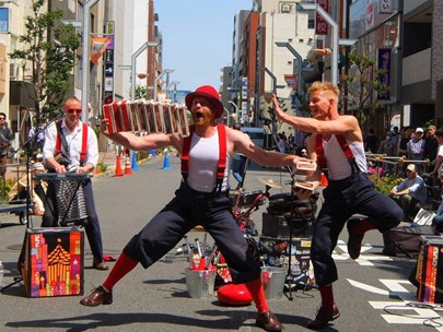Three acrobats / street musicians performing in a street with very little crowd at the moment of the photo