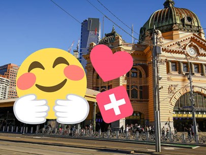 Image of Flinders St Station with 3 stickers. One is a yellow smiling face. One is a pink heart. One is a white cross on a red background