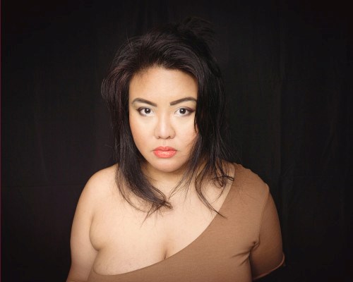 Headshot of Angela wearing a brown dress with one breast partially exposed