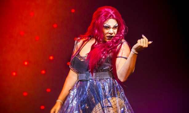 Woman on stage beckoning to approach her; red lighting with stars behind