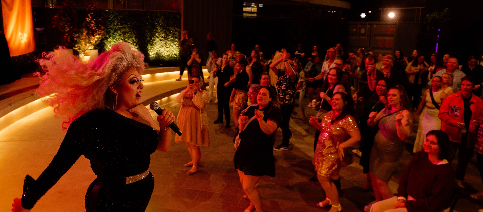 A drag queen singing to a crowd at an outdoor dance party at night